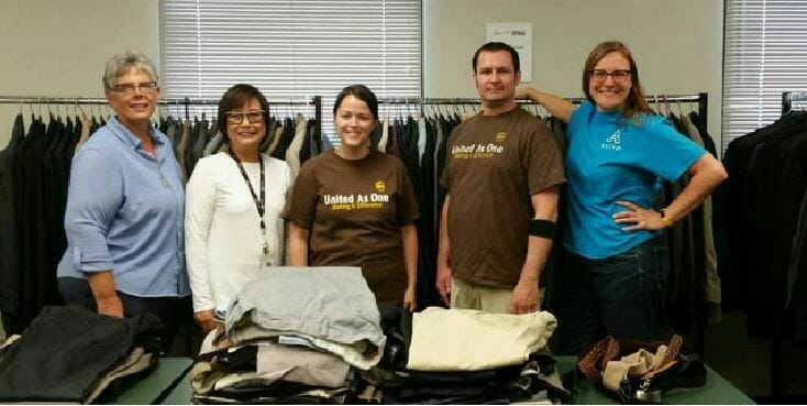 UPS volunteers and Avivo staff pose in front of one section of suits at Men's Wearhouse Suit Giveaway