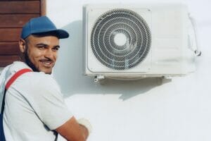 HVAC installer poses for photo while installing air conditioner.