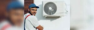A smiling man works on an air conditioner in this image.