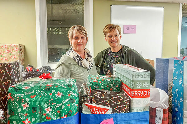 Two volunteers for Adopt-A-Family at Avivo pose for a photo in front of gifts for program participants they've received.