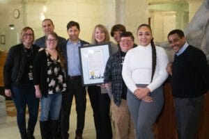 Group of Avivo staff, Minneapolis Mayor Jacob Frey, an Avivo program participant, Wildflyer Coffee staff, and City of Minneapolis staff pose for a photo at Minneapolis City Hall.