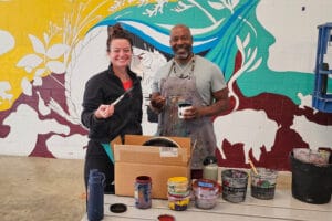 Photo of two artists taking a break and posing while helping paint a mural at Avivo Village.
